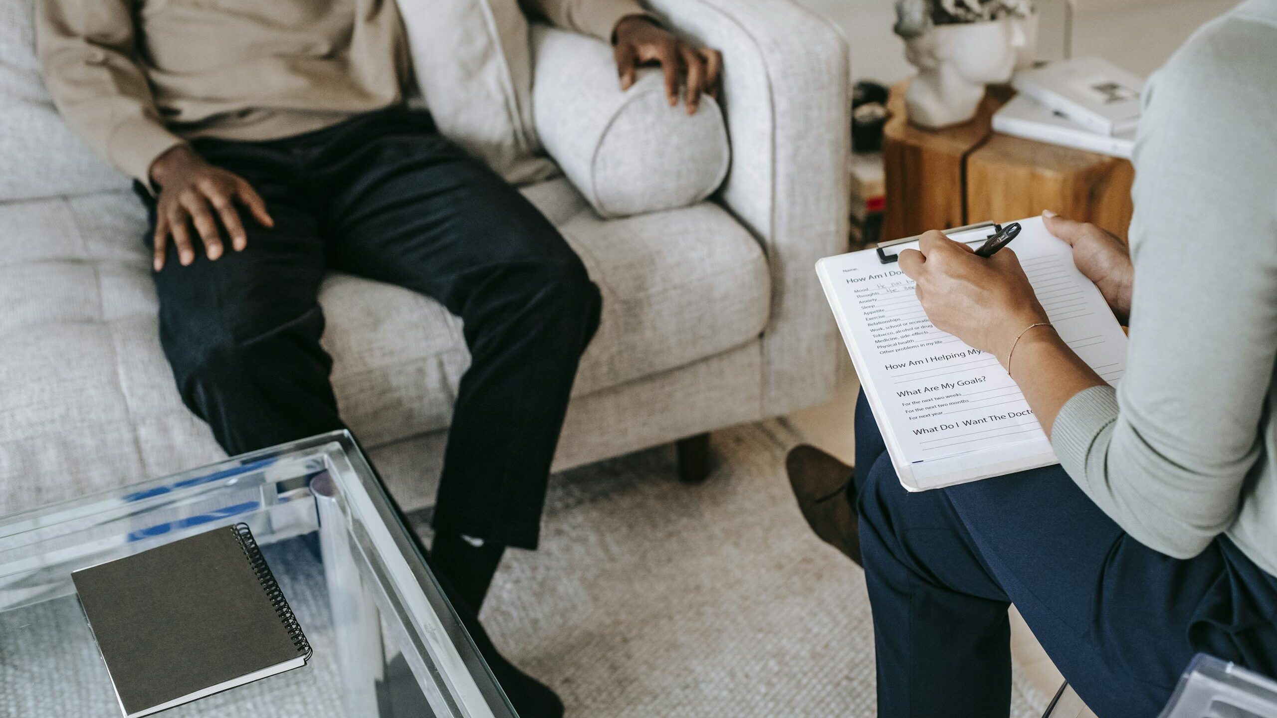 From above crop African American male in casual clothes sitting on comfy couch and answering professional female consultant questions in modern psychotherapy office